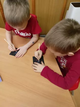 Chłopcy na czarnych karteczkach malują kolorowe serduszka.