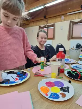 Dziewczynka klei bałwanka na talerzyku papierowym.