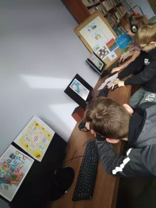 Dwóch chłopaków i dziewczyna siedzą przed komputerami w bibliotece.