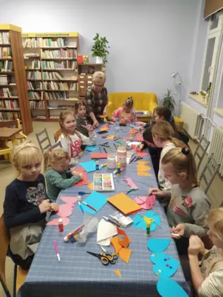 Dzieci siedzą przy stole i wykonują prace plastyczne.