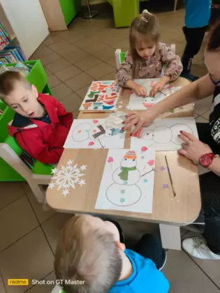 Przedszkolaki ubierają bałwanki wyciętymi elementami ubrania.