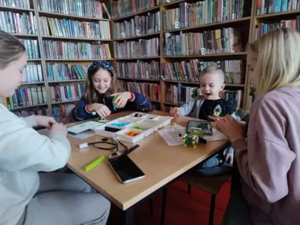 Dzieci siedzą przy stoliku i składają klocki Lego.