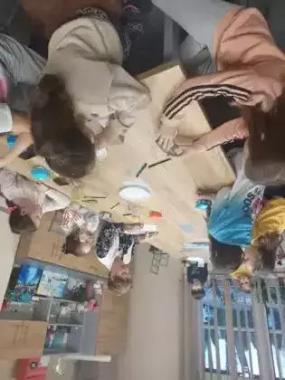 Uczestnicy zajęć literacko-plastycznych siedzą przy stole i wykonują magiczne pudełeczka metodą origami