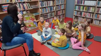 Dzieci siedzą na dywanie i słuchają czytanej bajeczki.