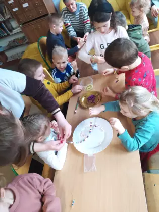 Uczestnicy zajęć nawlekają koraliki na sznurek.