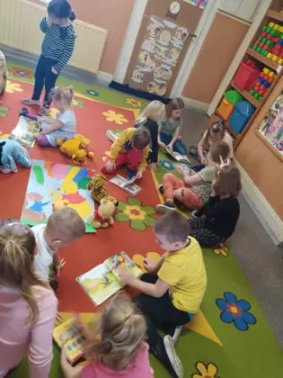 Przedszkolaki na dywanie oglądają książeczki.