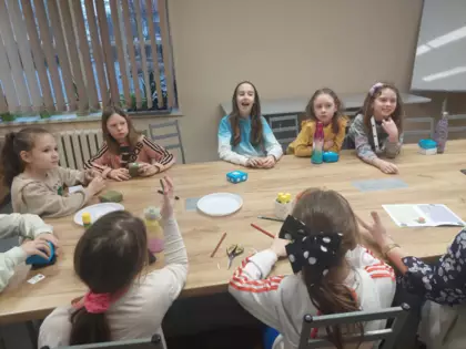 Uczestnicy zajęć literacko-plastycznych siedzą przy stole i wykonują magiczne pudełeczka metodą origami.