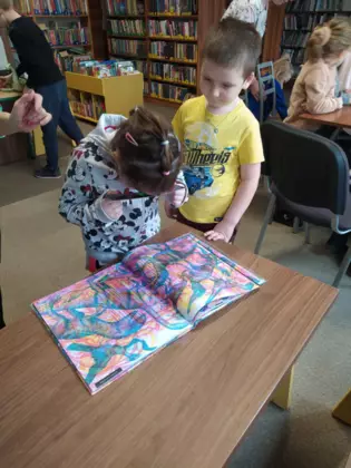 Dzieci oglądają kolorową książeczkę o dinozaurach.