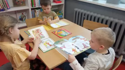 Dzieci siedzą przy stoliku i kolorują obrazek.