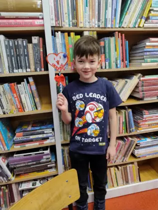 Chłopczyk prezentuje swoje serduszko walentynkowe z papieru.