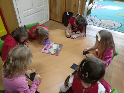 Dziewczynki w przedszkolu siedzą przy stoliku i kolorują obrazki.