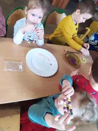 Dzieci nawlekają kolorowe koraliki na sznurek.