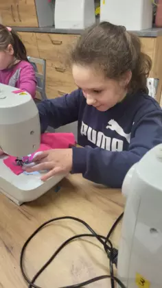 Dziewczynka siedzi przy maszynie i szyje piórnik.