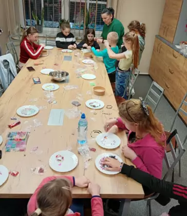 Uczestnicy przy wspólnym stole wykonują bransoletki i wisiorki z koralików.