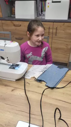 Dziewczynka siedzi przy maszynie i szyje piórnik.