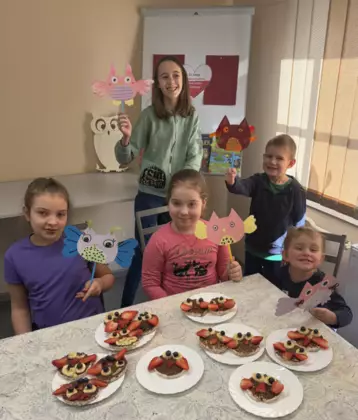 Uczestnicy po skończonych zajęciach pozują do zdjęcia w rękach trzymając sowy a przed nimi na stole leża na talerzykach sówki z wafli ryżowych.