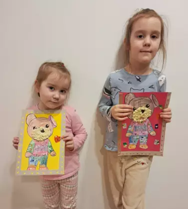 Dwie dziewczynki pokazują swoje prace plastyczne.