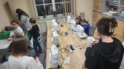 Uczestnicy zajęć siedzą przy maszynach do szycia i szyją workoplecaki.