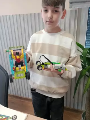 Uczestnik zajęć prezentuje na zdjęciu zbudowane przez siebie pojazdy.