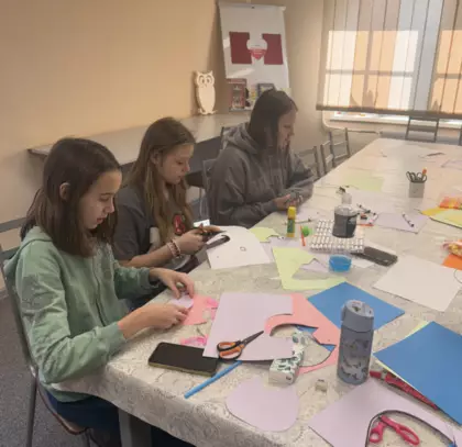 Uczestniczki na zajęciach literacko-plastycznych wykonują kolorowe sówki z papieru.