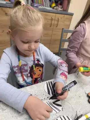 Dziewczynka maluje paski na zebrze z papieru.