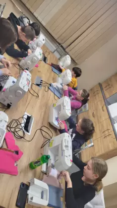 Dzieci siedzą przy maszynach i szyją.