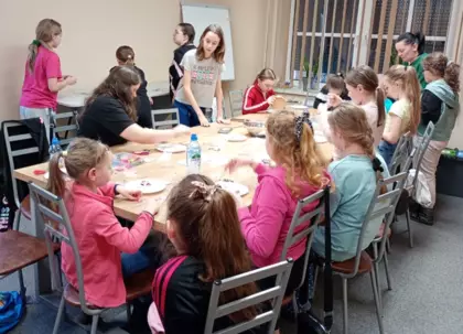 Uczestnicy przy wspólnym stole wykonują bransoletki i wisiorki z koralików.