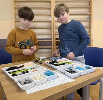 Chłopcy budują z klocków lego samochodziki.