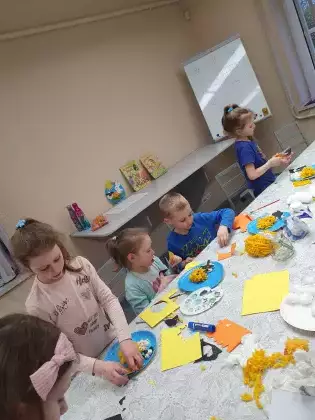 Dzieci przy stole wykonują prace plastyczne.