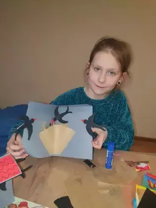 Dziewczynka trzyma w ręce wykonaną pracę plastyczną z papieru