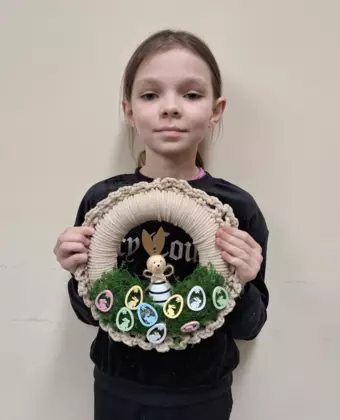 Dziewczynka trzymająca w ręce zrobiony na szydełku wianek wielkanocny.