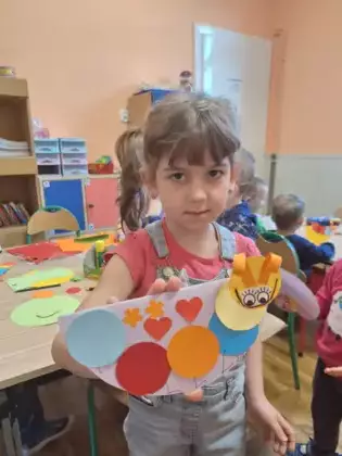 Dziewczynka trzyma w ręce pracę plastyczną przedstawiającą stonogę.