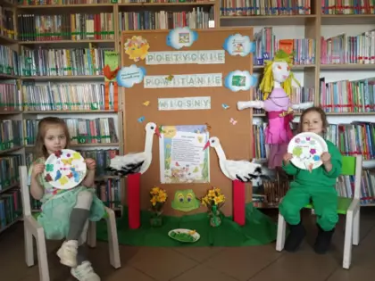 Dwie dziewczynki przedstawiają swoje wiosenne talerzyki na tle dekoracji związanej z poetyckim powitaniem wiosny