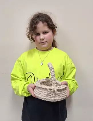 Dziewczynka trzymająca w ręce zrobiony na szydełku koszyczek wielkanocny.