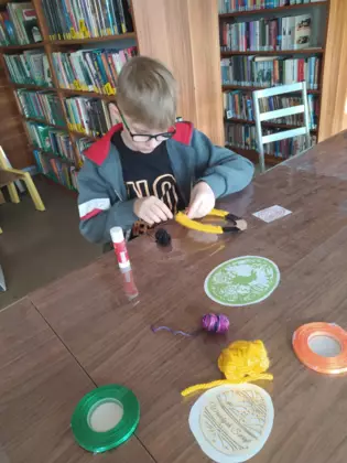 Chłopak okleja włóczką wielkanocne jajko.