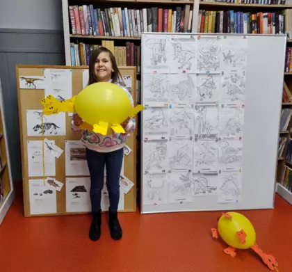 Dziewczynka na tle tablic ze swoim balonowym dinozaurem.