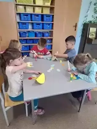 Przedszkolaki siedza przy stoliku i wycinają kolorowe kółeczka.