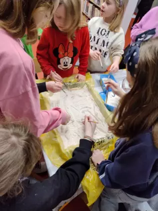 Dzieci pędzelkami wykopują skamieniałości dinozaura z mąki.