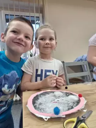 Chłopczyk i dziewczynka oklejają kulę kolorowymi pomponami.