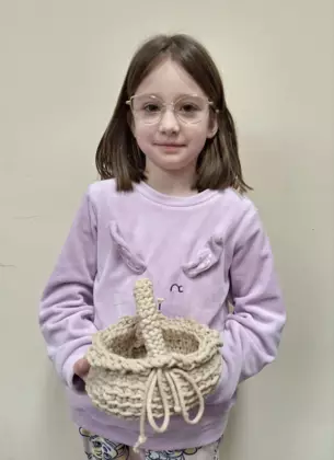 Dziewczynka trzymająca w ręce zrobiony na szydełku koszyczek wielkanocny.