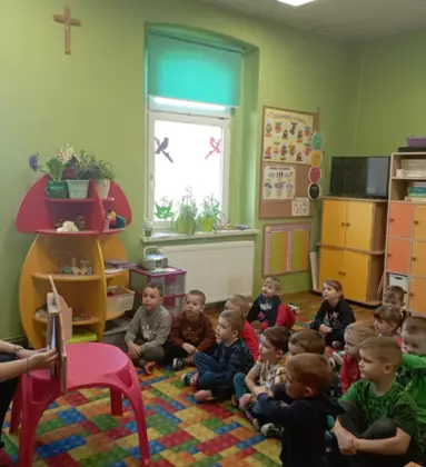 Przedszkolaki słuchaja opowiadania czytanego za pomocą teatrzyku kamishibai.