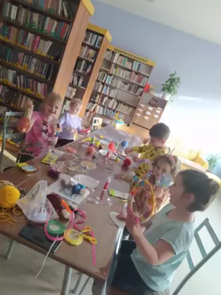 Przedszkolaki oklejają wielkanocne jajko kolorową włóczką.