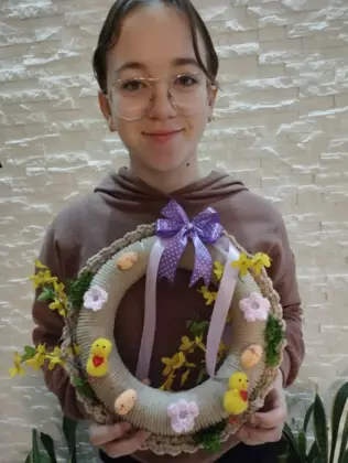 Dziewczynka trzymająca w ręce zrobiony na szydełku wianek wielkanocny.