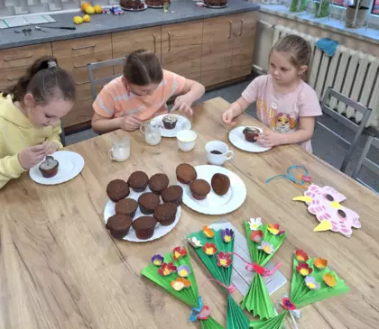 Dzieci dekorują lukrem i posypką babeczki.