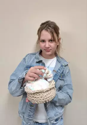 Dziewczynka trzymająca w ręce zrobiony na szydełku koszyczek wielkanocny.