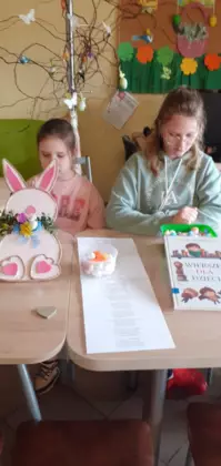 Dziewczyny słuchają opowiadania . Na stole przed nimi leży zajączek wielkanocny.