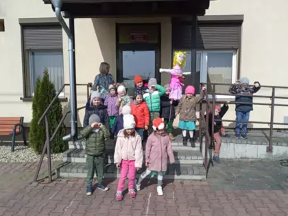 Grupa dzieci poazuje do zdjęcia przed biblioteką w Kośmidrach