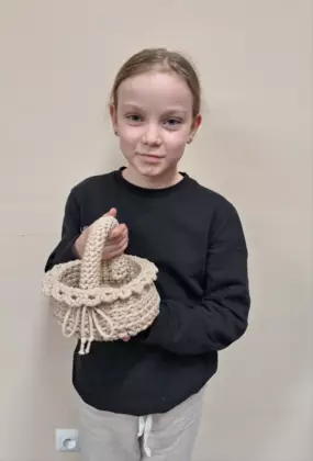 Dziewczynka trzymająca w ręce zrobiony na szydełku koszyczek wielkanocny.