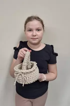 Dziewczynka trzymająca w ręce zrobiony na szydełku koszyczek wielkanocny.