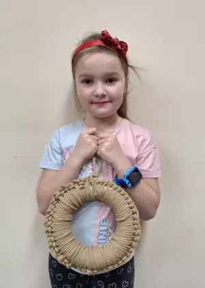 Dziewczynka trzymająca w ręce zrobiony na szydełku wianek wielkanocny.